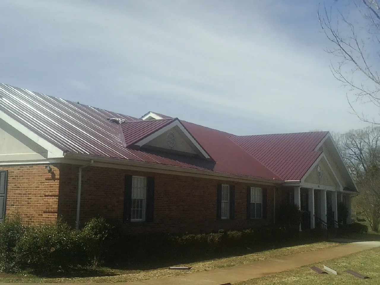 Red metal roof with gabled entries on a long brick building, from a Hail Damage Roof Repair job in Maury City