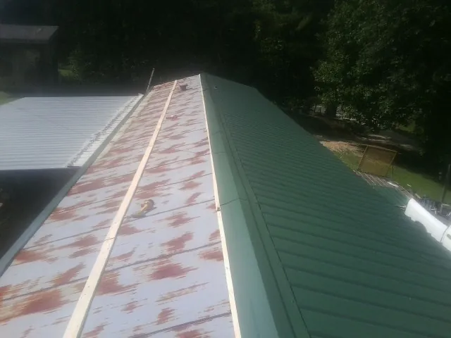 Old rusted panels beside newly installed green metal roofing — Wind Damage Roof Repair by Roofing Brothers in Maury City