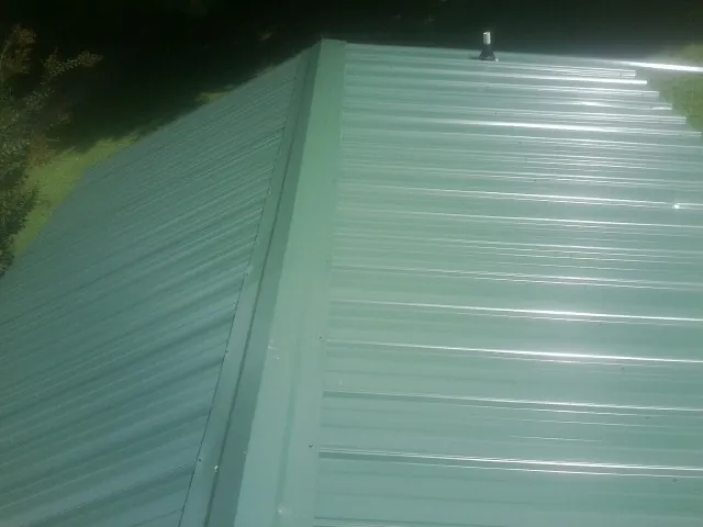 New green metal panels meeting at the ridge of a roof — Flat Roof Repair work by our crew in Maury City