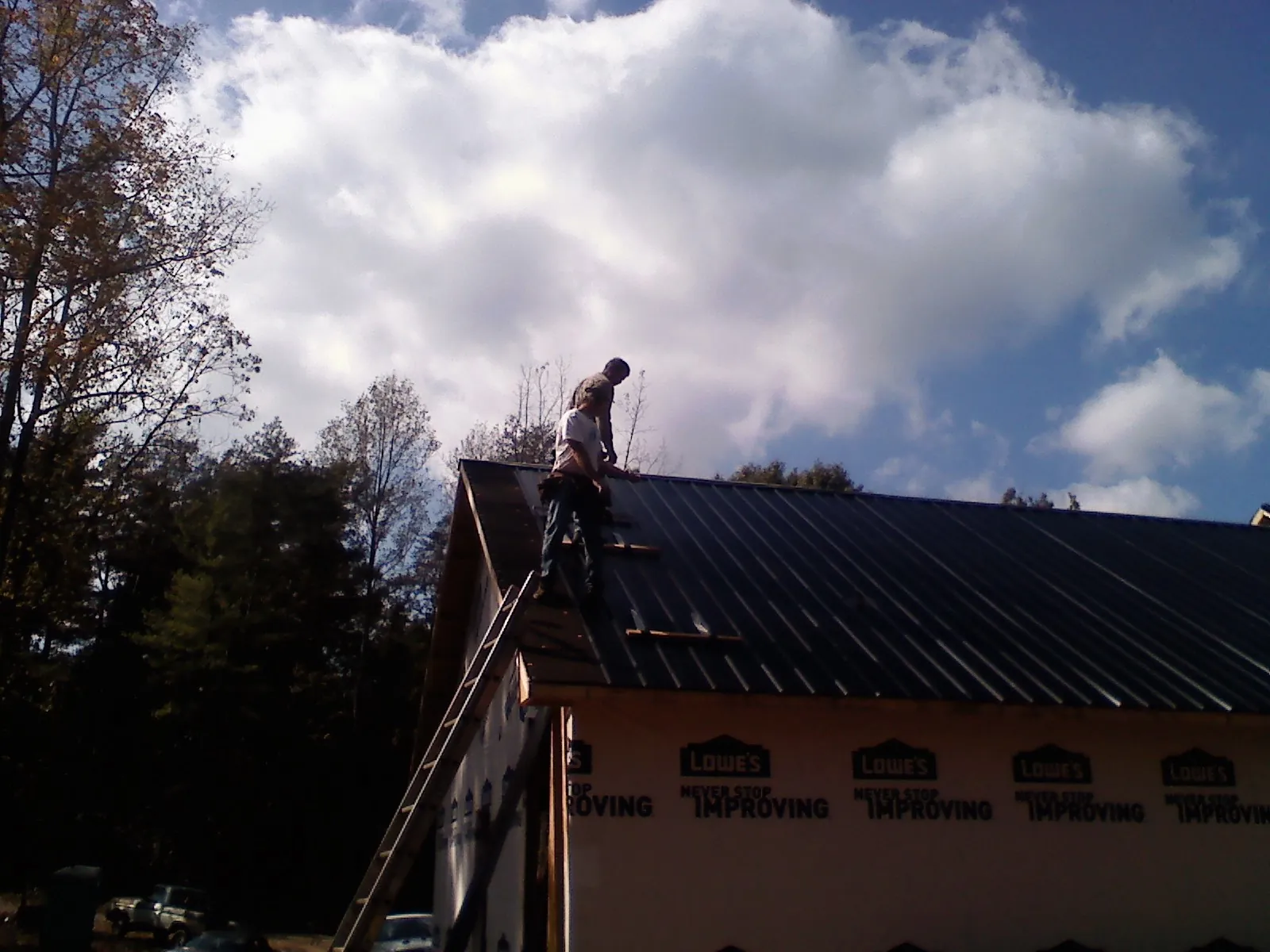 Roofer fastening dark metal panels high against a cloudy sky, from a Roof Inspection job in Maury City