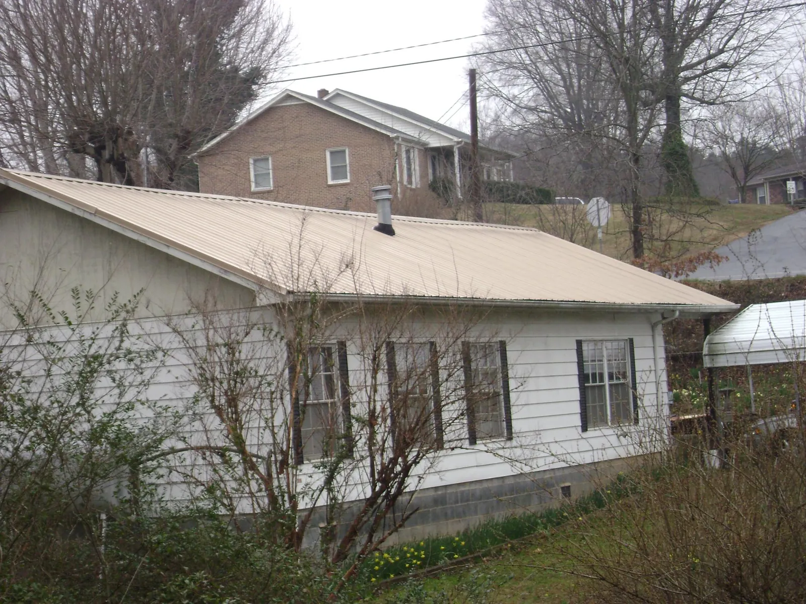 Tan metal roof on a white sided house set into a hillside — Commercial Roofing by Roofing Brothers in Maury City