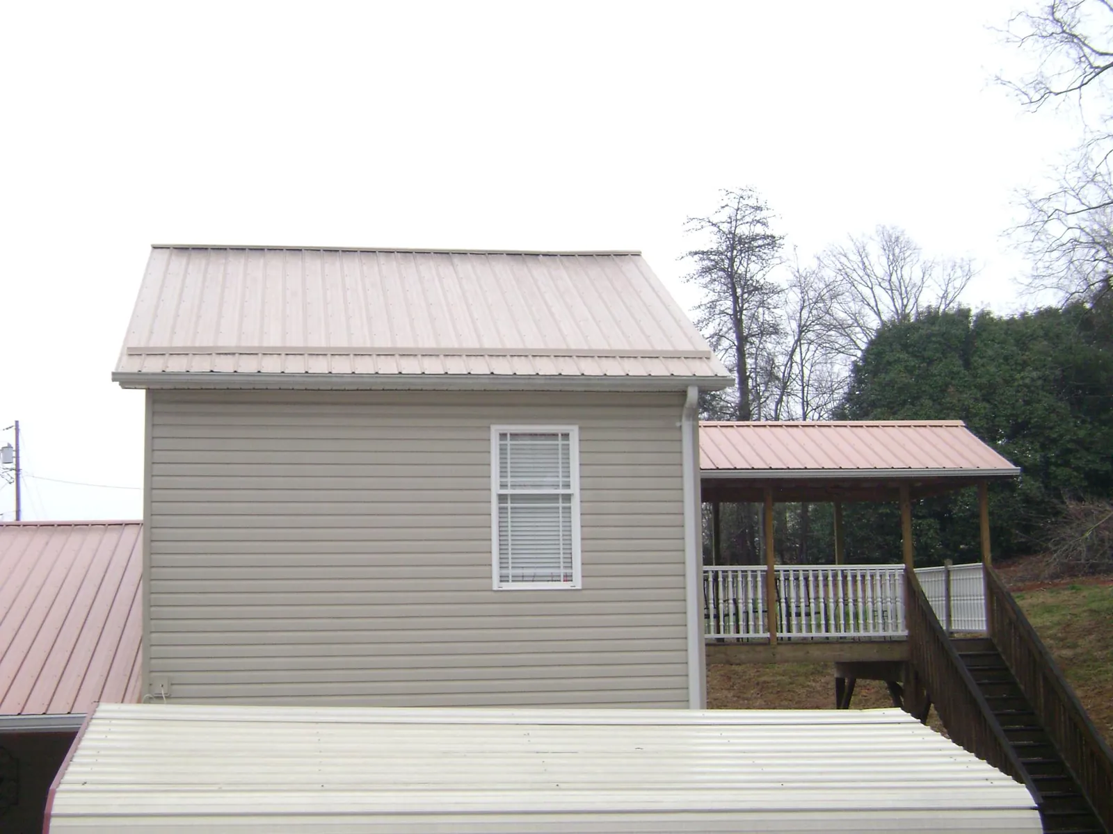 Tan metal roofs on a two story addition and attached porch, from a Roof Replacement job in Maury City